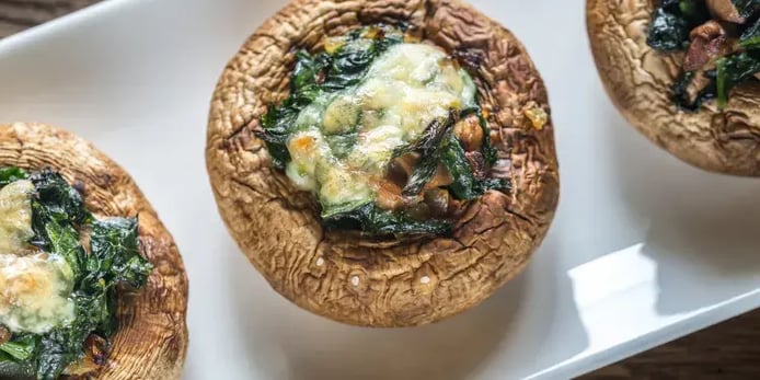 A close up photo of a large grilled mushroom with garlic, spinach, tomatoes and blue cheese on top.