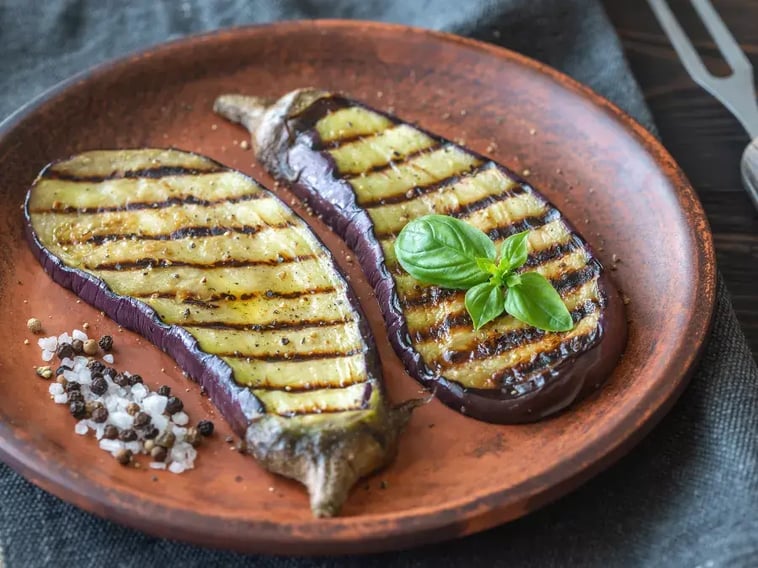 Chargrilled aubergine pieces on plate with basil sprigg