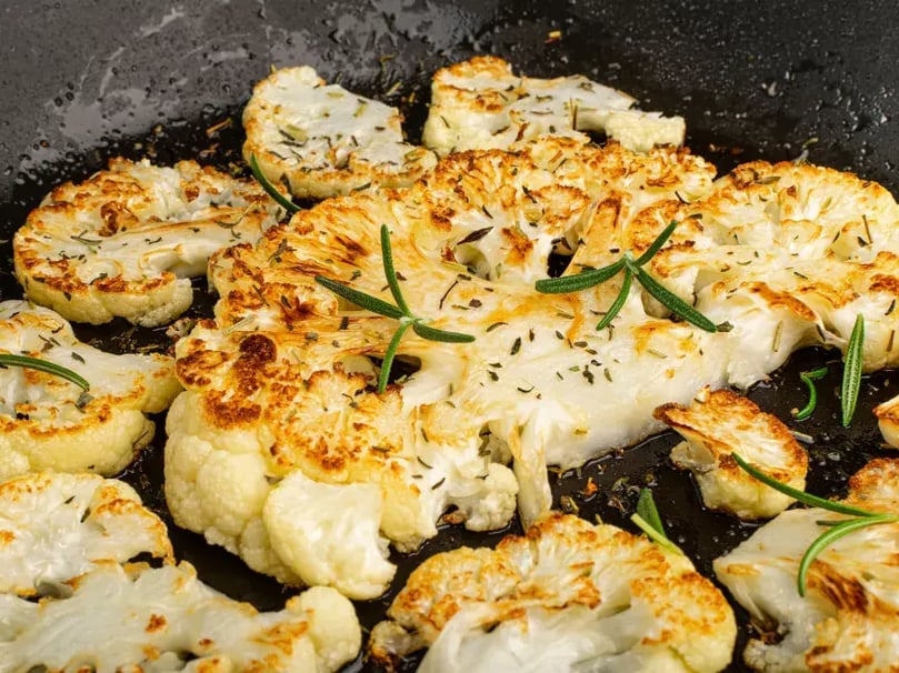 BBQ Chargrilled cauliflower pieces on wooden chopping board with rosemary