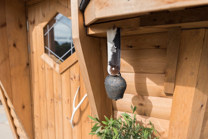 A cow bell handing outside the door of a BBQ cabin.