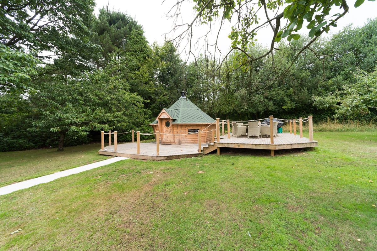 A 17m2 barbeque hut with an extension on a wooden patio. To the right of the cabin is a rattan outdoor didning set.