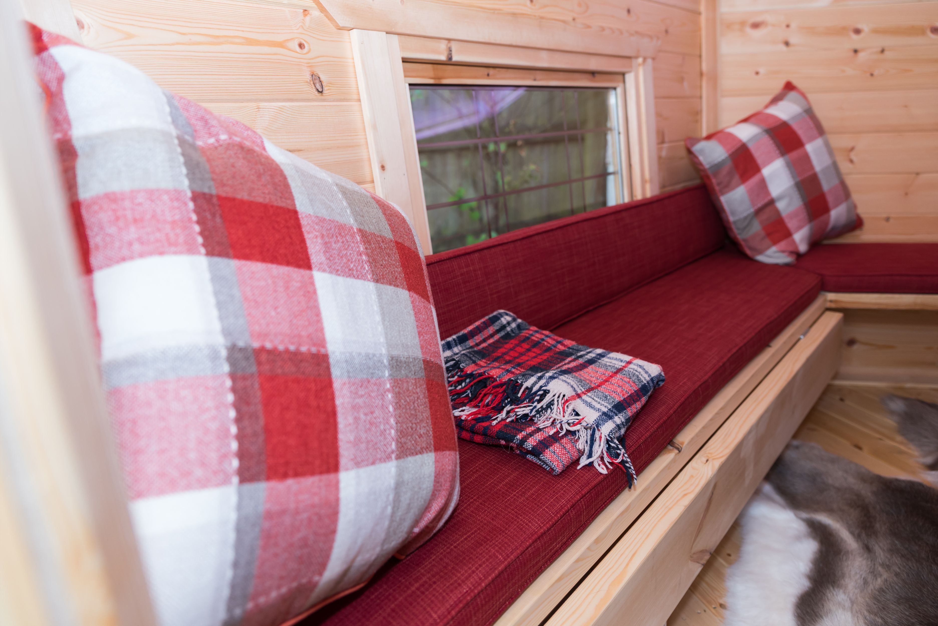 Red pillows and checkered throw cushions on a bench in a wooden BBQ hut.