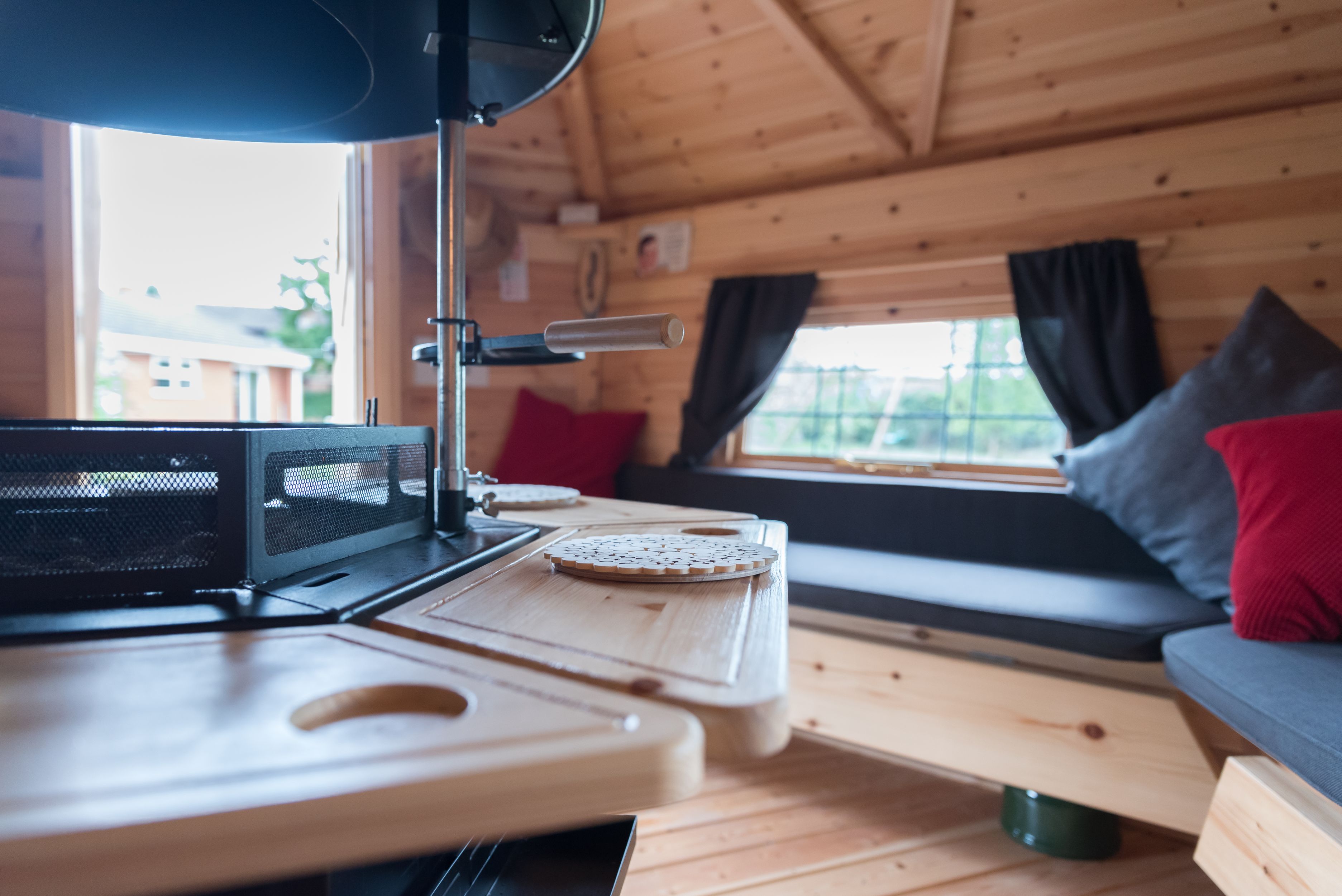 A close up of the wooden bench surrounding an indoor BBQ grill. The benches around the grill have navy and red pillows and throw cushions.