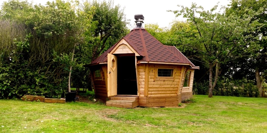 Exterior of a wooden barbecue house and extension surrounded by mature garden trees