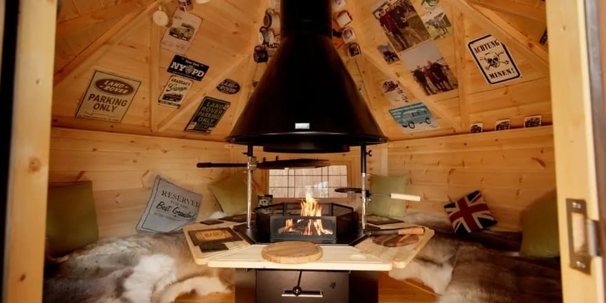 Land Rover-themed grill cabin with a central fire, wooden seating and cosy interior inside one of Arctic Cabins’ small BBQ huts.