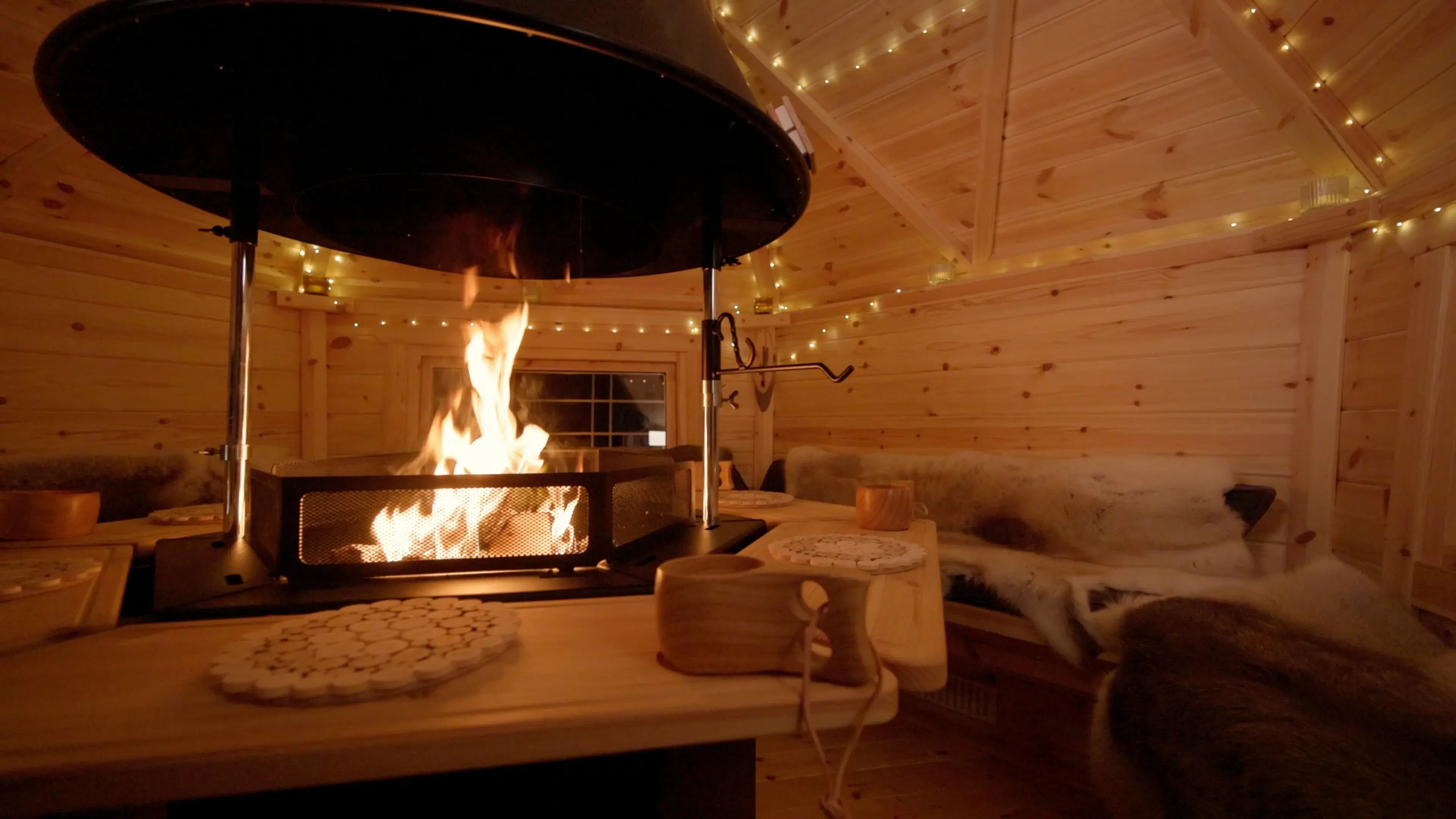 The interior of a 7m2 BBQ cabin, decorated with mini fairy lights and reindeer skins on the benches.