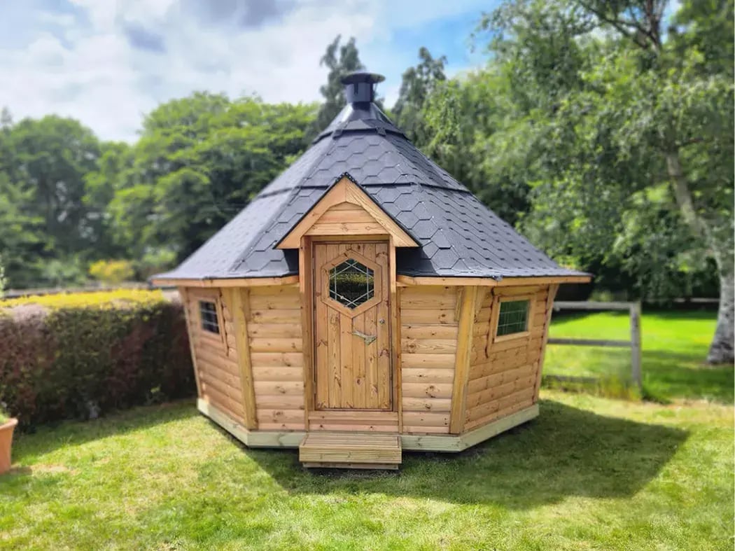 Wooden barbecue hut with a modern black roof set in a large green garden