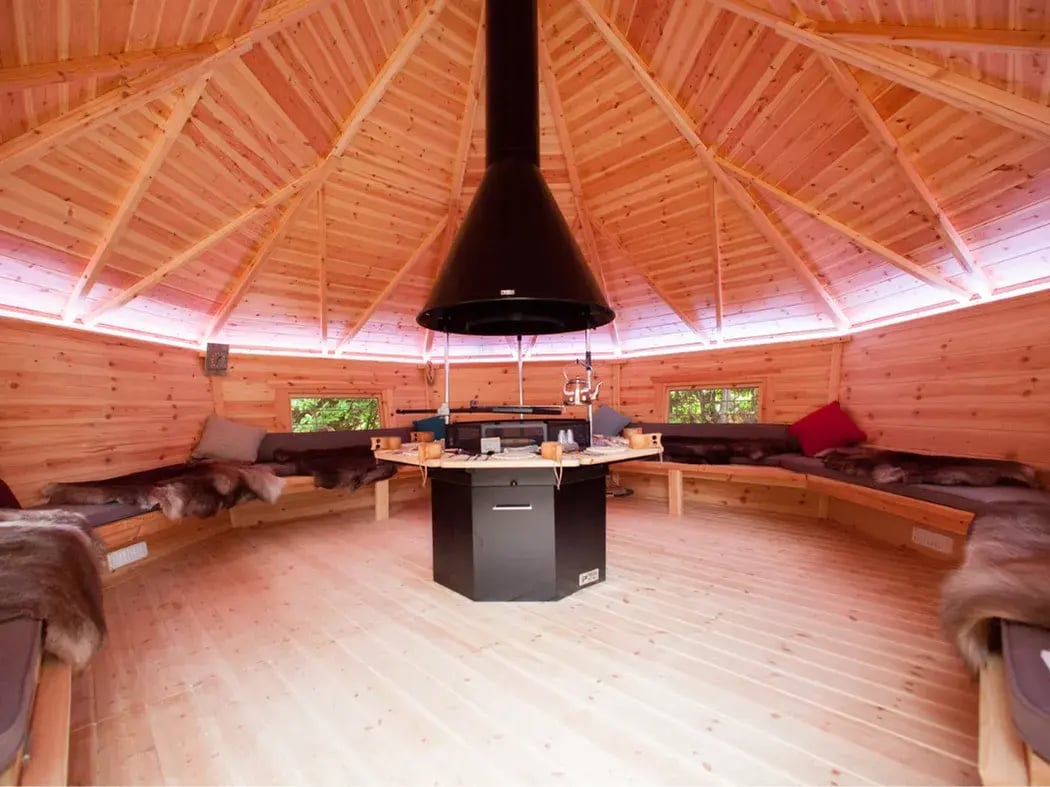 Scandinavian BBQ hut with central grill area and cosy wooden interior for outdoor dining
