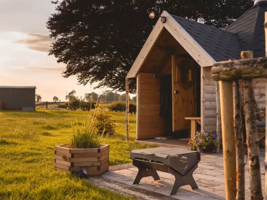 door to a luxury glamping pod with outdoor seating and sunrise 