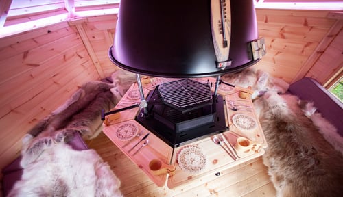 Inside a 7m² Arctic Cabin BBQ hut with central BBQ unit, placemats and cutlery seen