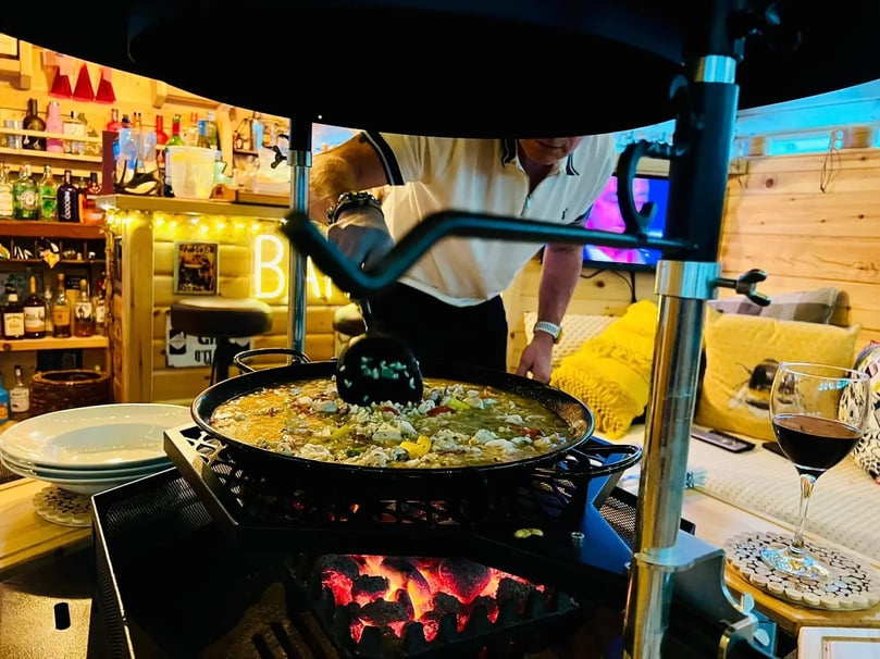 paella being stirred in pot over an bbq grill inside an arctic cabin