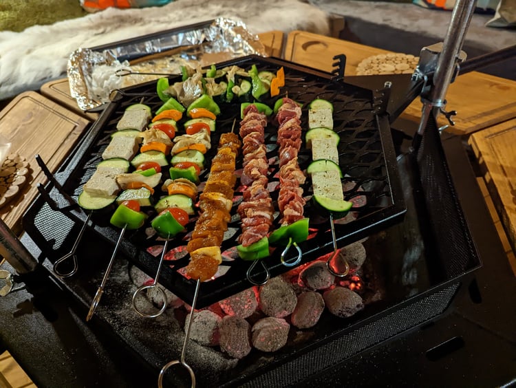 A mixture of lamb and pepper and tofu and zuccini skewers cooking over an indoor BBQ grill.