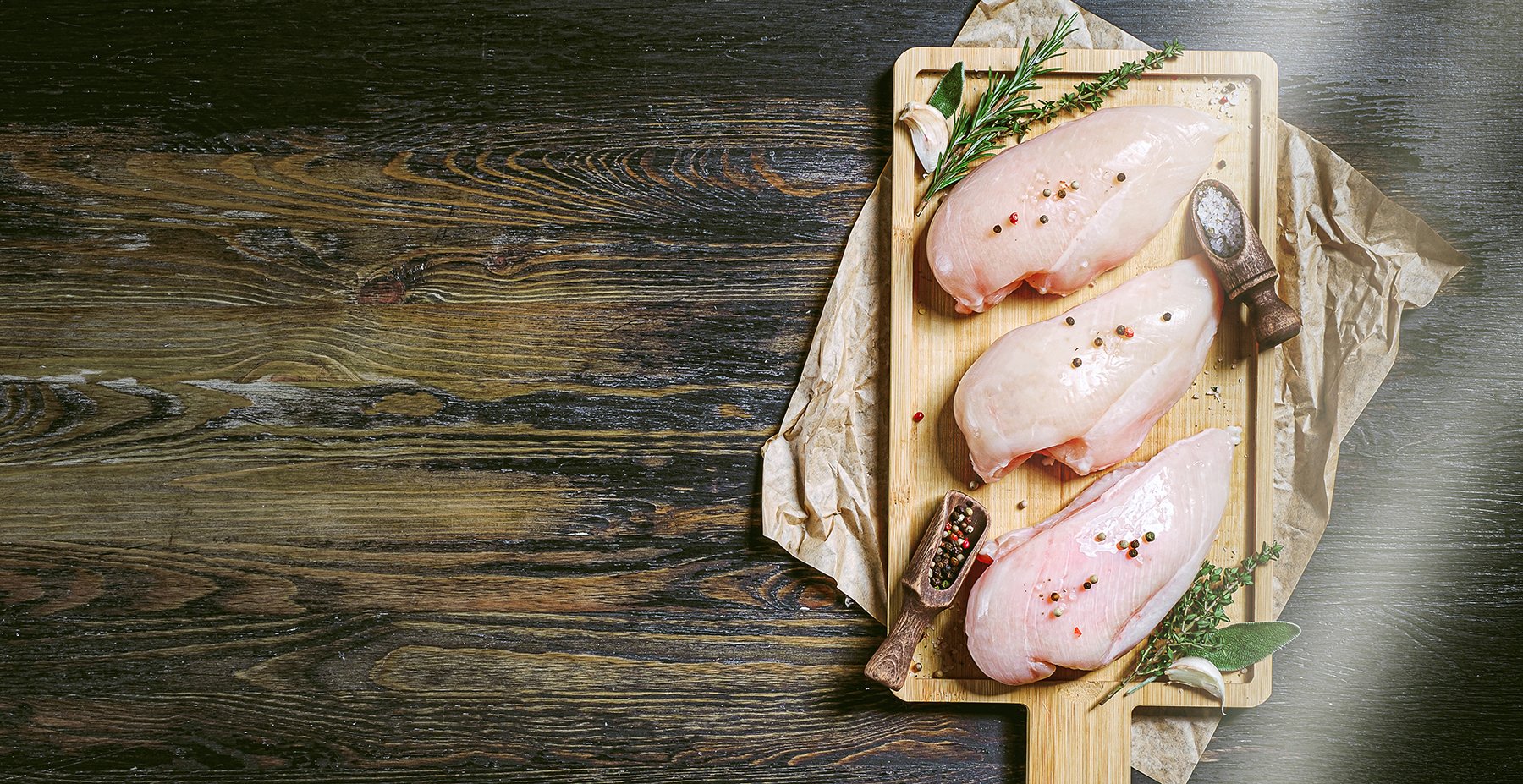 Chicken breasts marinading on wooden chopping board with spices and salt