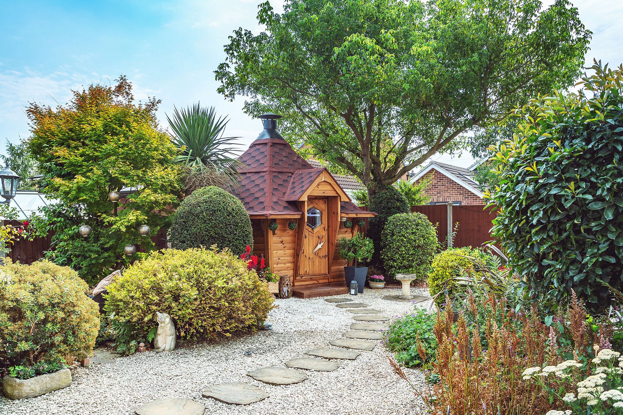 Exterior of an Arctic Cabins 10m² Grill House with red roof in a leafy garden setting