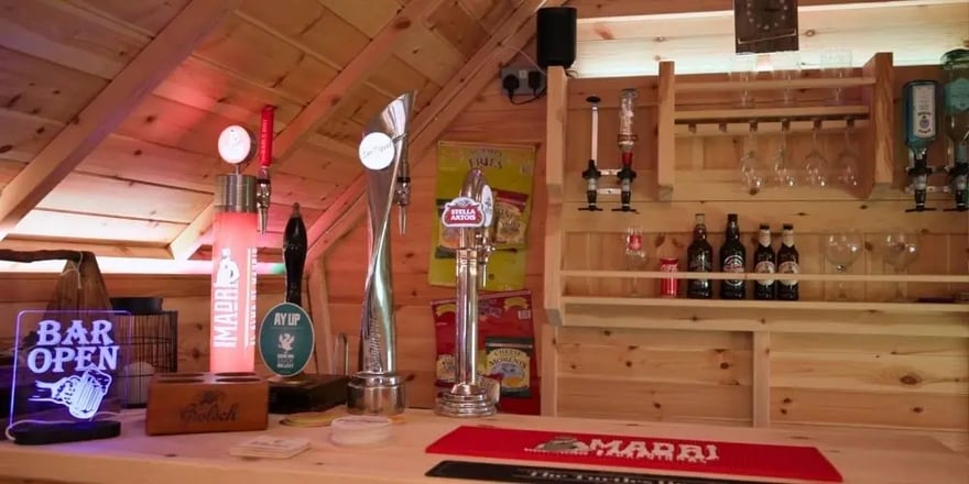 Large BBQ cabin interior featuring a fully stocked garden pub, wooden bar, beer taps and seating.
