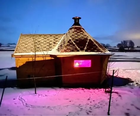 BBQ cabin with a rear extension in the snow. The cabin is emitting a pink light from inside.