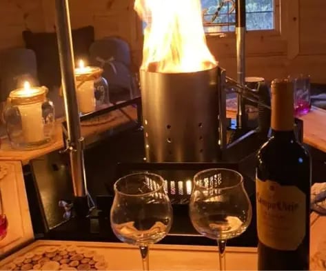 Inside a BBQ hut with a grill. There is a bottle of wine with two glasses on the table.