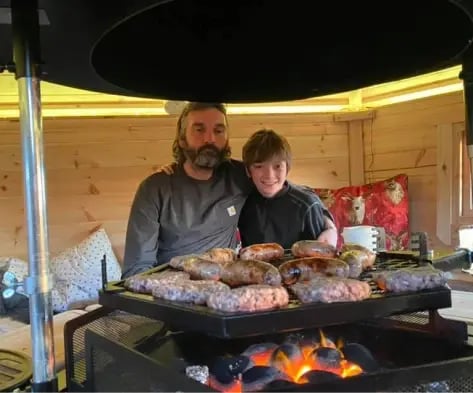 A parent and child cooking sausages in a Scandinavian BBQ hut
