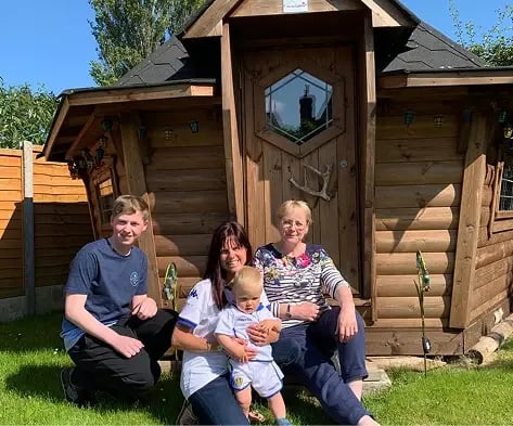 A family sat on the doorstep of a garden BBQ cabin
