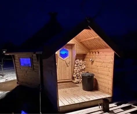 A BBQ cabin with a porch lit up at night.