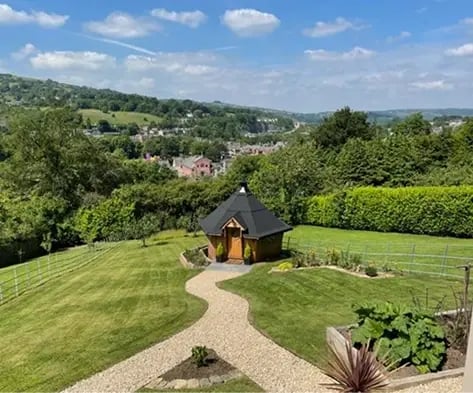 A barbeque cabin in a a large garden with a gravel path leading to the door.