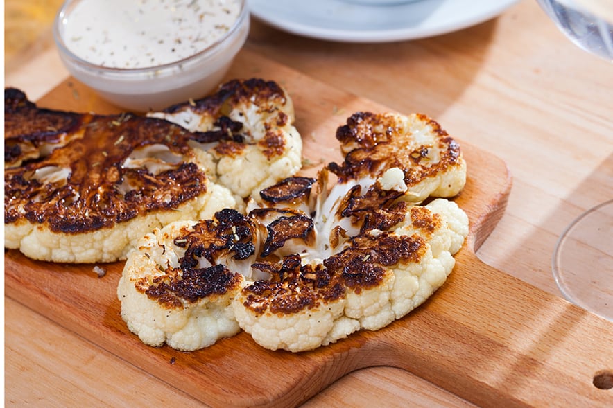 BBQ Chargrilled cauliflower pieces on wooden chopping board with dip