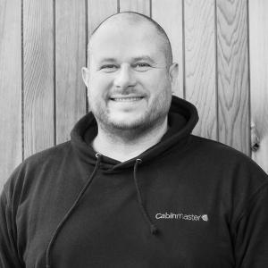 Black & White photo of Cliff Hickling, Head of Sales at Arctic Cabins in front of a cedar garden room by sister company Cabin Master