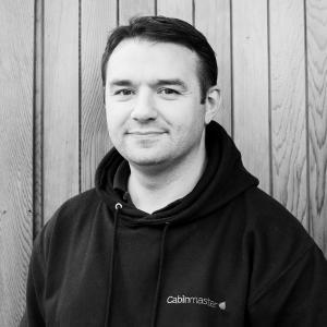 Black & White photo of Simon Lees, Sales Executive at Arctic Cabins in front of a cedar garden room by sister company Cabin Master