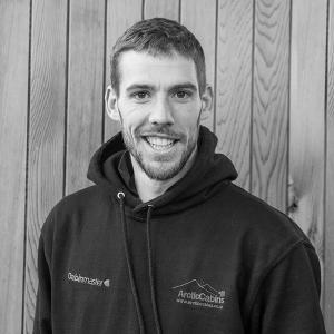 Black & White photo of Jamie Gillon, Installations Team Leader at Arctic Cabins in front of a cedar garden room by sister company Cabin Master