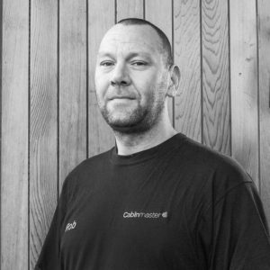 Black & White photo of Rob Lee, Head Of Installations at Arctic Cabins in front of a cedar garden room by sister company Cabin Master